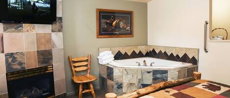 Ein Schlafzimmer mit Kamin, Fernseher, einer großen Badewanne und einer gesteppten Bettdecke.