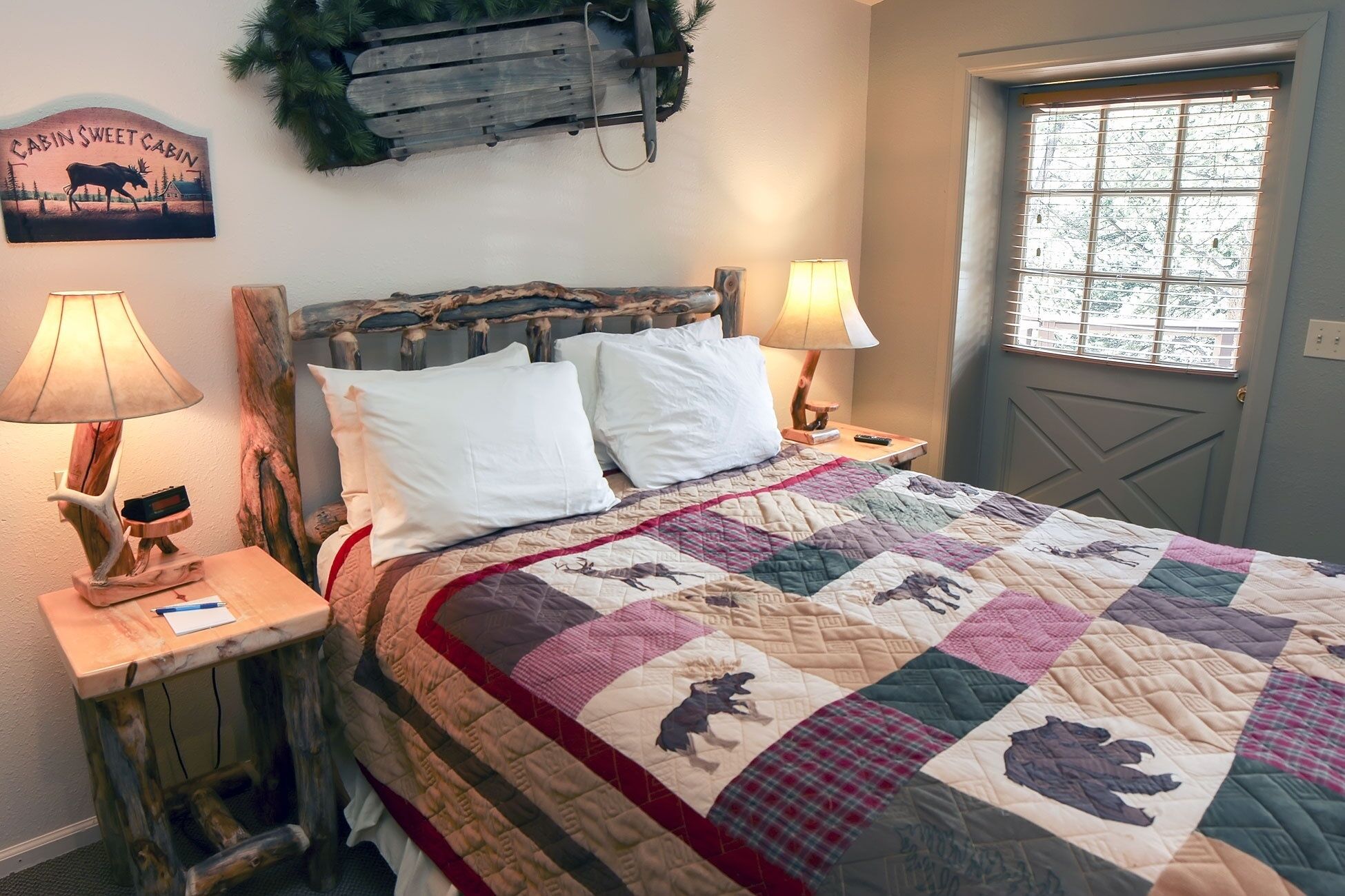 Un dormitorio con cabecera de madera, dos lámparas de noche, colcha con estampados de animales, una puerta con ventanal y un cartel sobre la cama.