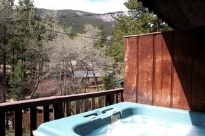 Eine Holzterrasse mit Whirlpool und Blick auf einen Wald und Berge.
