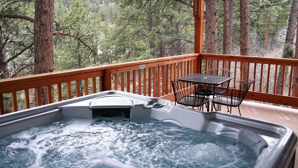 Un bain à remous sur une terrasse en bois, avec vue sur une forêt.