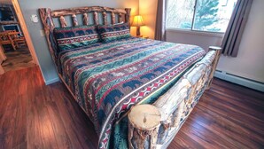 Un lit avec une tête de lit en bois, une couvre-lit à motifs et une fenêtre avec des rideaux.