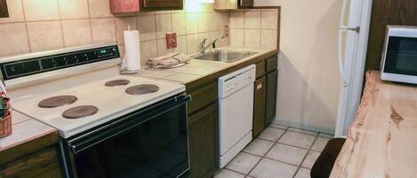 A compact kitchen with a stove, sink, and dishwasher.