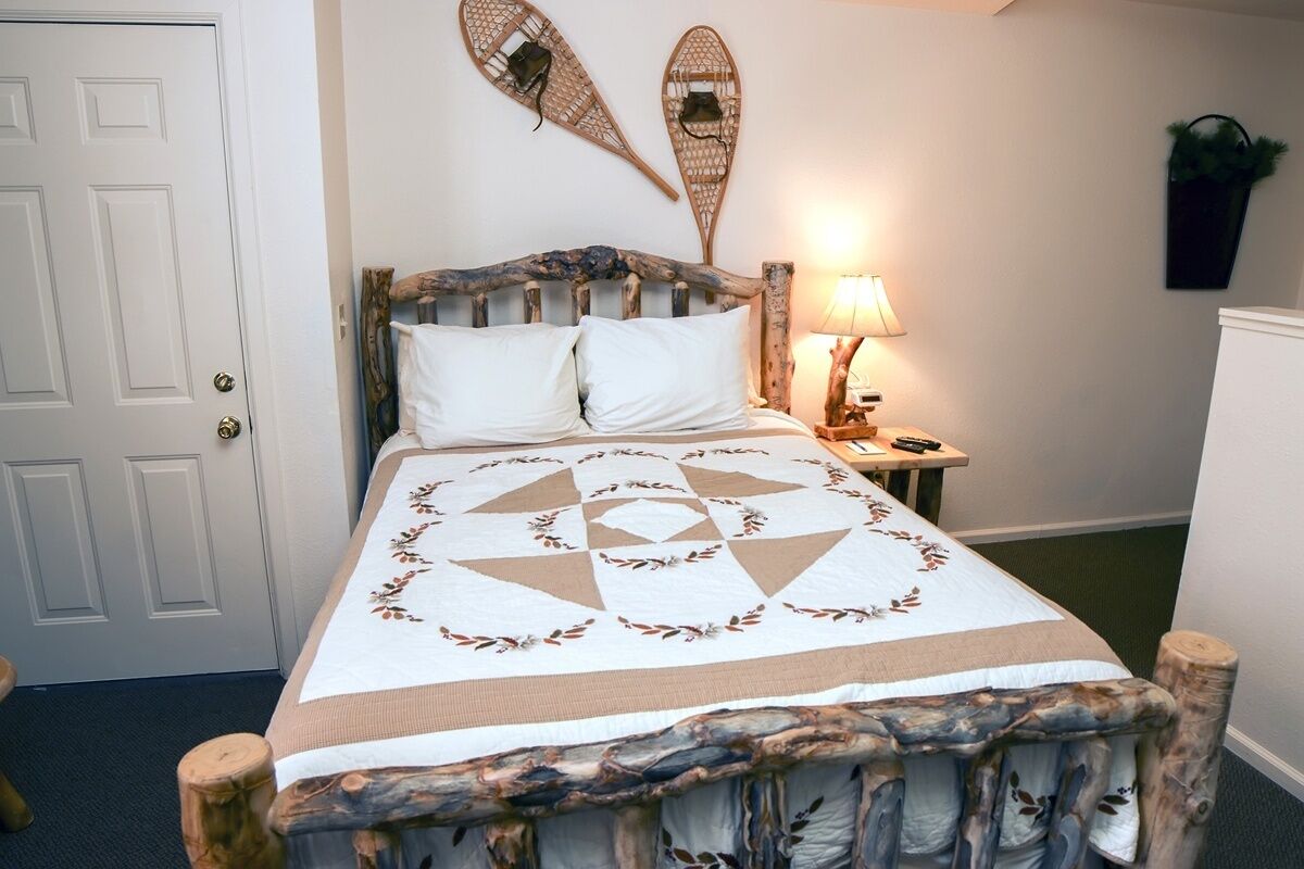 Een bed met een bedspreider met geometrisch patroon, een rustiek hoofdbord en twee decoratieve items aan de muur.