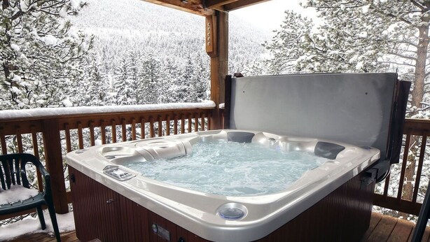 Un jacuzzi en una terraza de madera con vistas a árboles cubiertos de nieve.