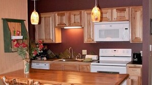 Une cuisine avec des meubles de rangement en bois, un micro-ondes blanc, une cuisinière et une table à manger en bois avec des chaises.