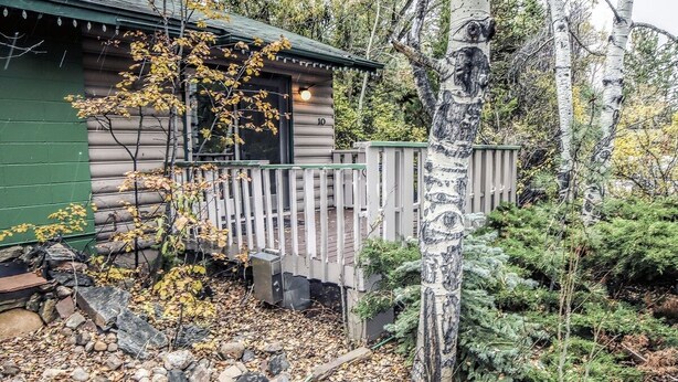 Eine Holzhütte mit einer Holzterrasse, umgeben von Bäumen und felsigem Untergrund.