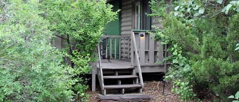 A cabin with a wooden staircase leading to a porch, surrounded by dense greenery.