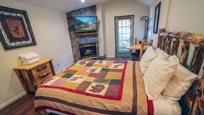 A bedroom with a large bed, a fireplace, a wooden headboard, and a quilted bedspread. - Fawn Valley Inn: 296 1 Bedroom Apts (Estes Park)