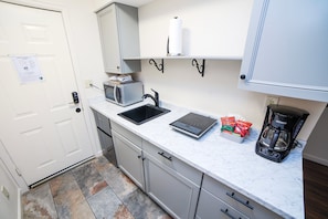 A compact kitchen with a microwave, sink, coffee maker, and a scale on the counter.