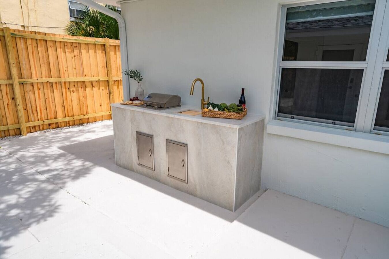 An outdoor kitchen area with a concrete countertop, two cabinets, a sink, and a faucet.