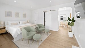 Une chambre moderne avec un lit, deux fauteuils, une petite table et une plante en pot.