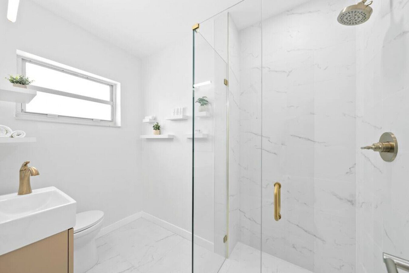 Ein modernes Badezimmer mit einer Duschkabine aus Glas, einem goldenen Wasserhahn und Marmorwänden.