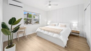 A modern bedroom with a large bed, a desk, and a potted plant.