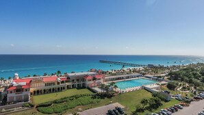 A resort with a swimming pool, a pier extending into the ocean, and a large building with a red roof.