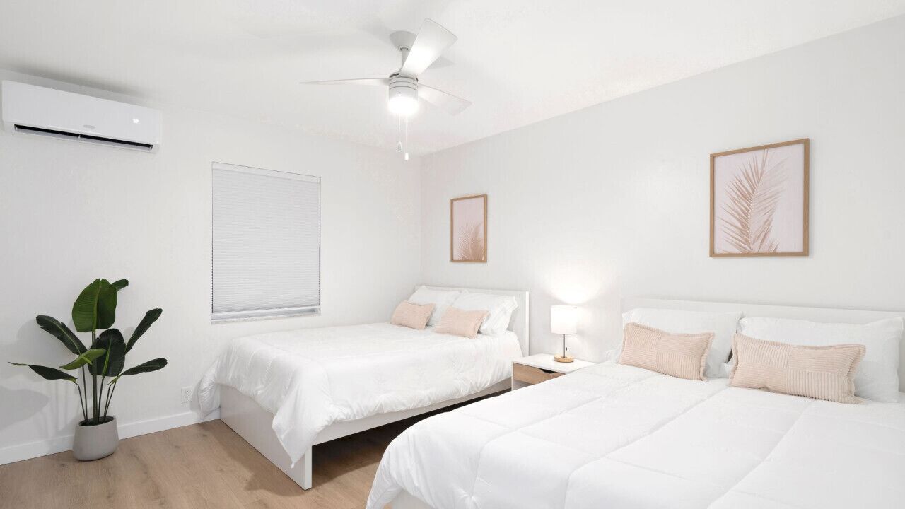 Une chambre d’hôtel avec deux lits, un ventilateur de plafond, un climatiseur, une fenêtre avec des stores et une plante en pot.