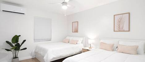 Une chambre d’hôtel avec deux lits, un ventilateur de plafond, un climatiseur, une fenêtre avec des stores et une plante en pot.