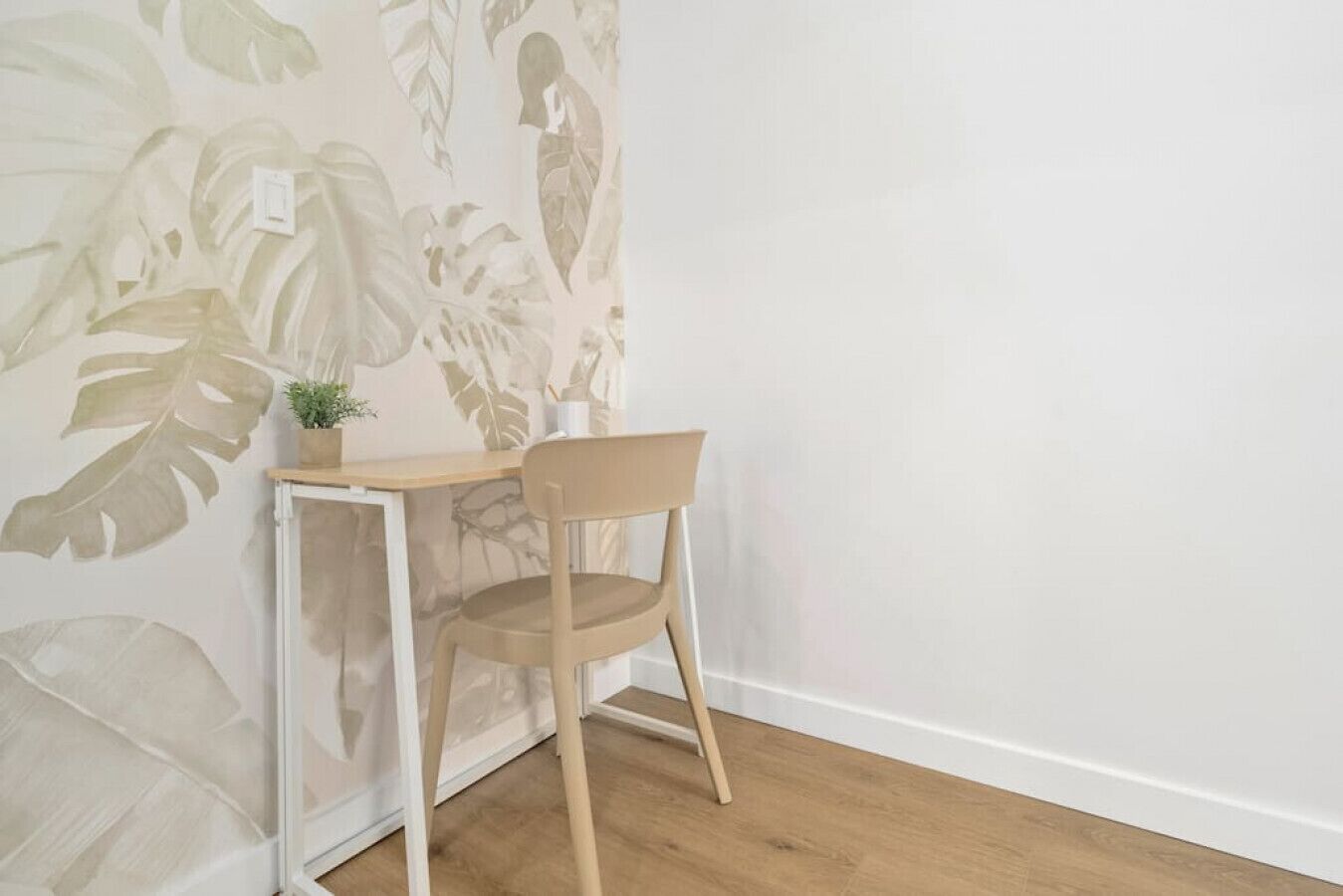 Un coin de pièce avec un plancher en bois, un bureau à cadre blanc et une chaise.