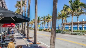 A seaside restaurant with outdoor seating, palm trees, and a view of the ocean. - Cute Retro Studio King Bed & Workspace - Villa 10 (Lake Worth)