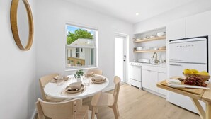 A modern kitchen with white cabinets, a built-in oven, and a refrigerator. There is a dining table with chairs and a window with a view of a house. - New 2 double beds -Near Golf & Beach - Villa 8 (Lake Worth)