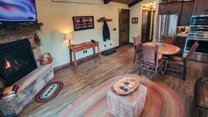 Ein gemütliches Wohnzimmer mit Kamin, Holzboden, einer Essecke mit rundem Tisch und einer Küche mit modernen Geräten.