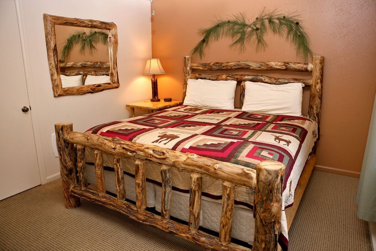 Een slaapkamer met een rustiek houten bed en een geborduurd quilt, en een spiegel met weerspiegeling van een palmboom.