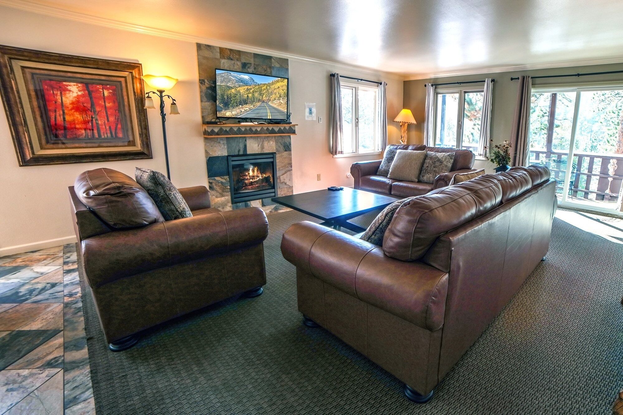 A living room with leather sofas, a fireplace, a television, and a view of the outdoors.
