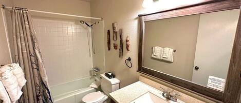 A bathroom with a bathtub, toilet, sink, and a large mirror.