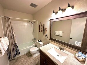 Un baño con bañera, inodoro, lavabo y un espejo grande.