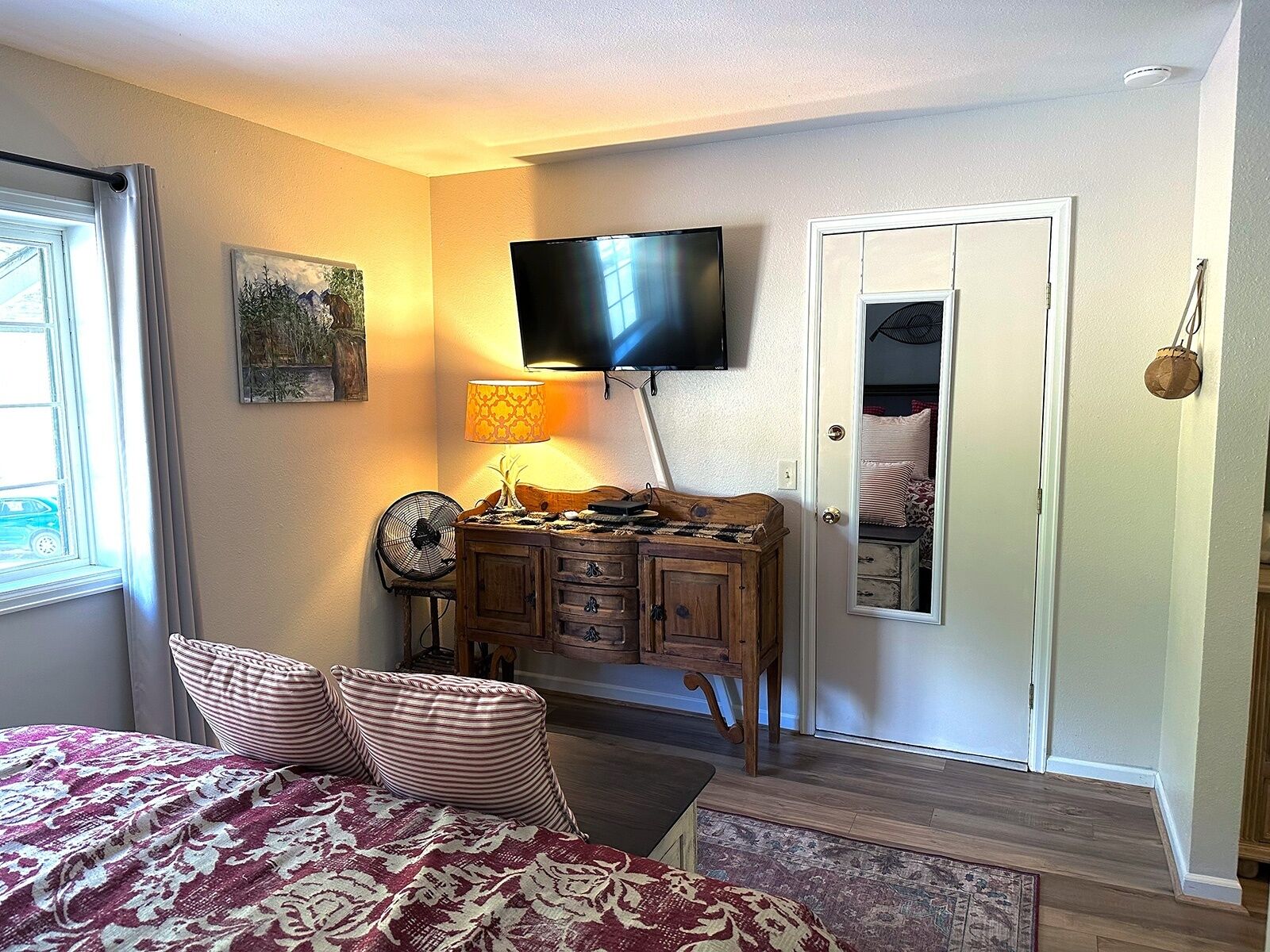 A bedroom with a bed, a dresser, a TV, a fan, and a door.