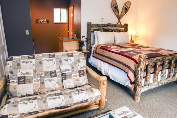 A cozy room with a wooden bed, a quilted chair, and a sign reading "Welcome to The Mountains".
