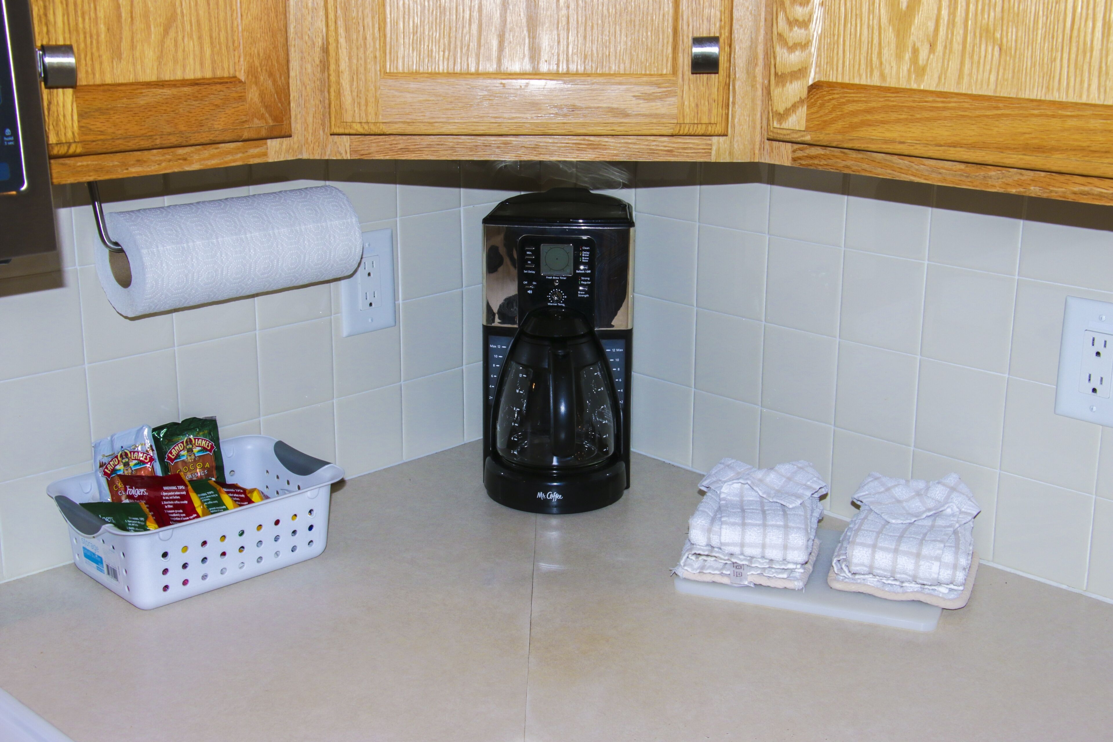 A kitchen with wooden cabinets, a coffee maker, a basket of coffee pods, and a roll of paper towels.