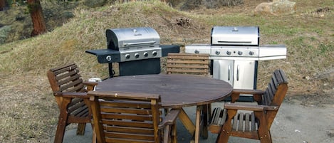 Un espace extérieur aménagé pour les repas, avec une table ronde et des chaises en bois, entouré de deux barbecues.