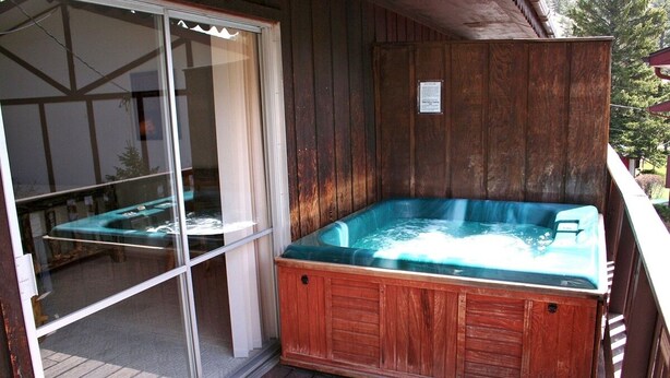A wooden deck with a hot tub, a sliding glass door, and a wooden wall. - Fawn Valley Inn: 256 1 Bedroom Apts (Estes Park)