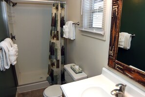 A bathroom with a shower, toilet, sink, and a mirror with a decorative frame. - Triple R Cottages: 3 1 Bedroom Cabin (Estes Park)