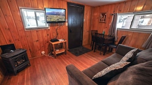 A cozy room with wooden walls, a TV mounted on the wall, a wooden table with chairs, a sofa, and a wood-burning stove. - Triple R Cottages: 3 1 Bedroom Cabin (Estes Park)