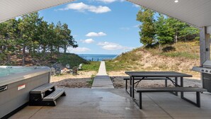 Ein überdachter Außenbereich mit Whirlpool, Grill, Picknicktisch und einem Weg zum Strand.