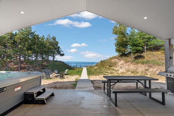 A covered outdoor area with a hot tub, grill, picnic table, and a pathway leading to a beach.