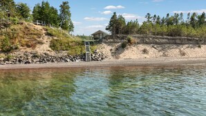 Ein Anwesen am Seeufer mit einer Holzhütte, einer Treppe zu einer Terrasse und freiem Blick auf das Wasser.