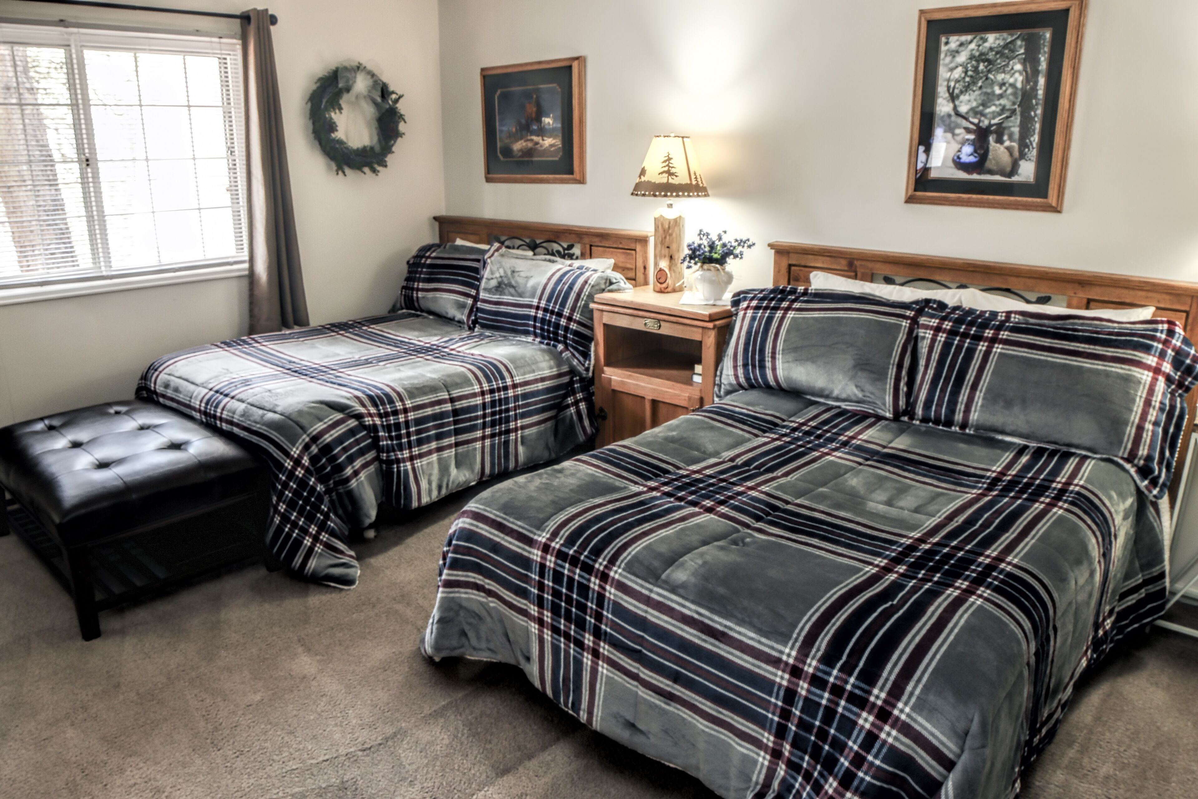 A bedroom with two beds, a nightstand, a lamp, and a window with blinds.