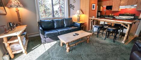 Ein gemütliches Wohnzimmer mit einer schwarzen Ledersofa, einem Holztisch und einer Küchenzeile mit Holzschränken und einer Mikrowelle.