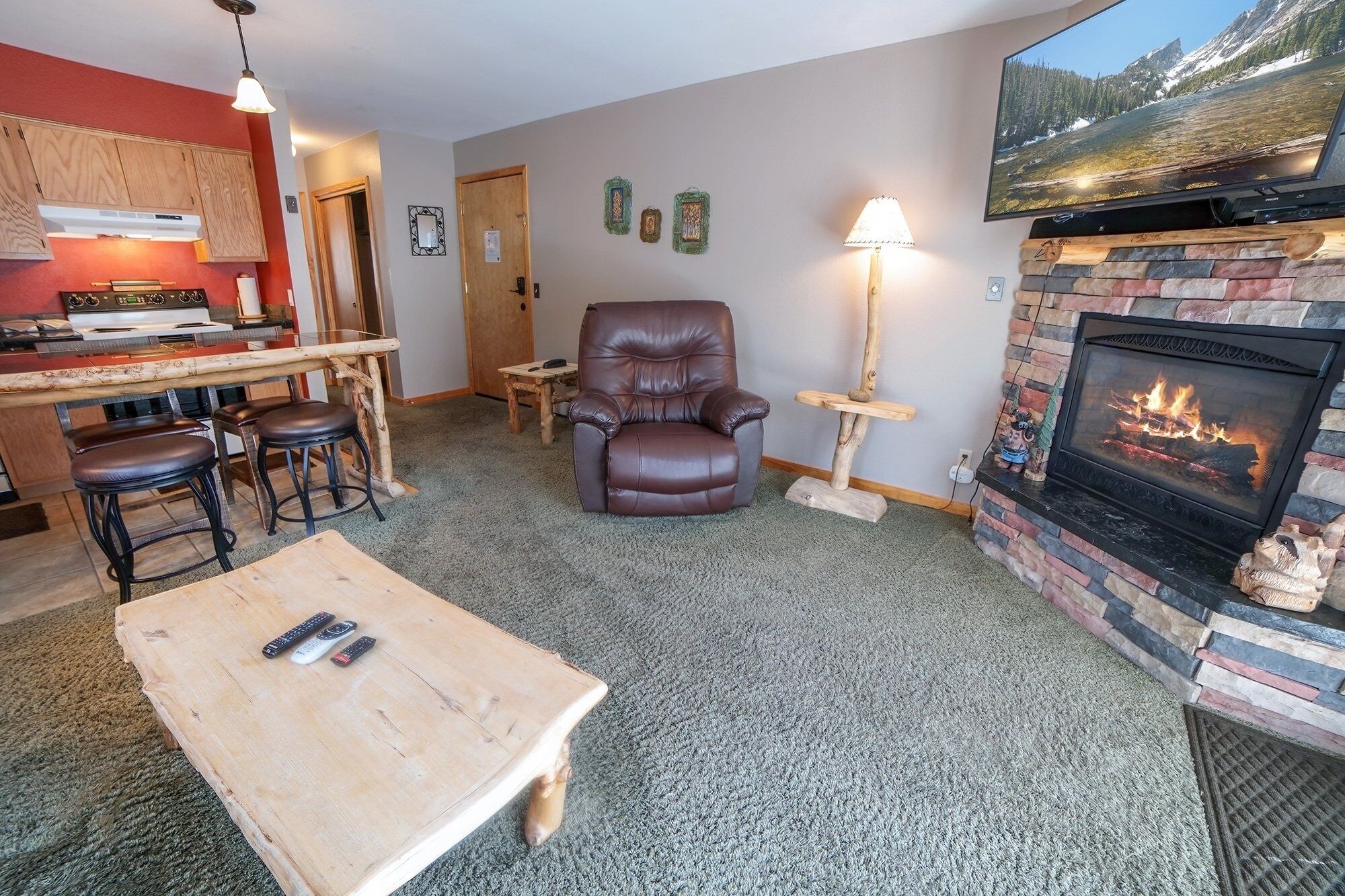 A cozy living room with a fireplace, a leather armchair, a coffee table, and a TV mounted on the wall.