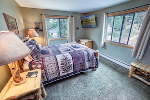 A bedroom with a bed, a nightstand, a lamp, and a window with a view of trees. - Fawn Valley Inn: 306 1 Bedroom Apts (Estes Park)