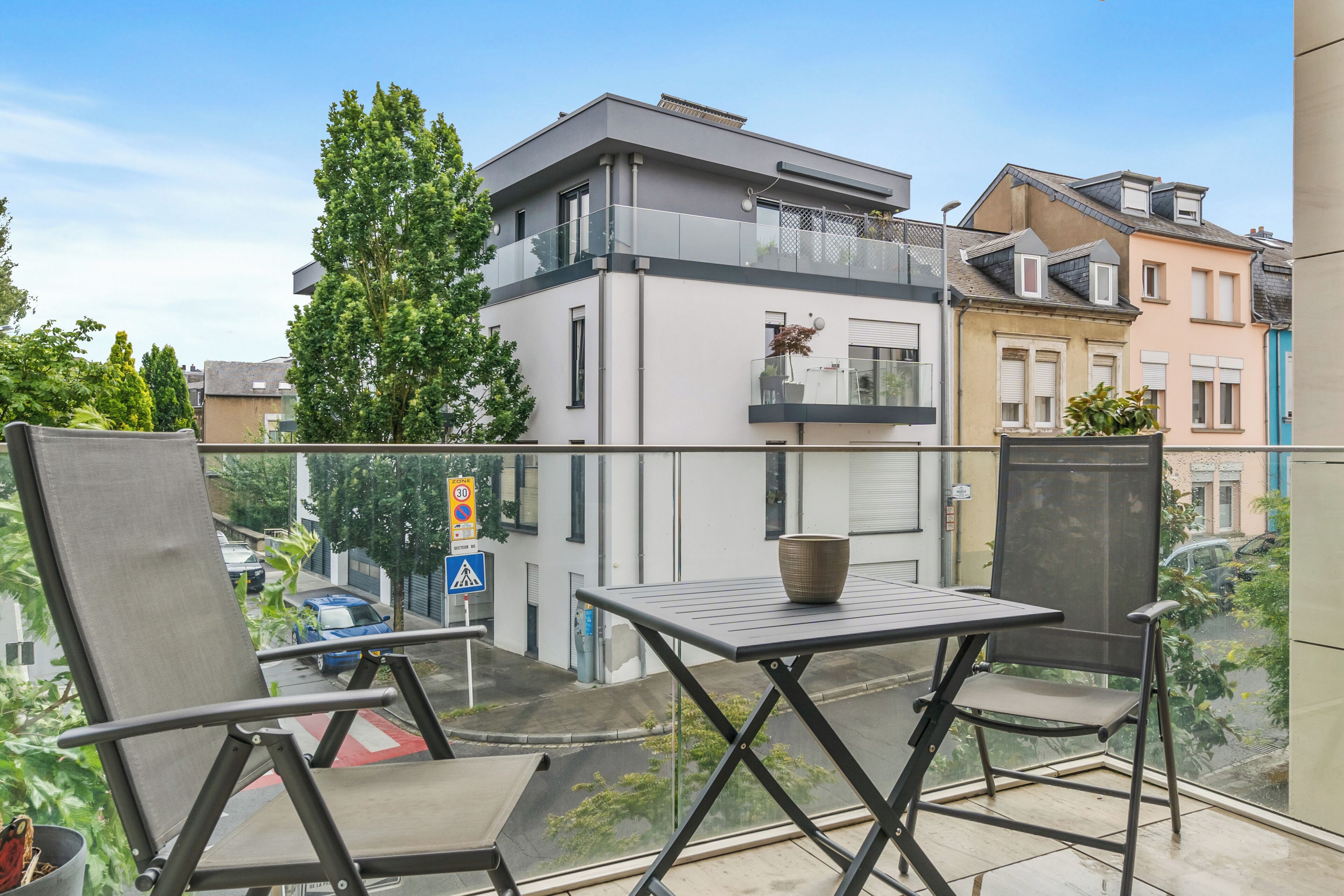 A balcony with a table and chairs, overlooking a street with buildings and cars.