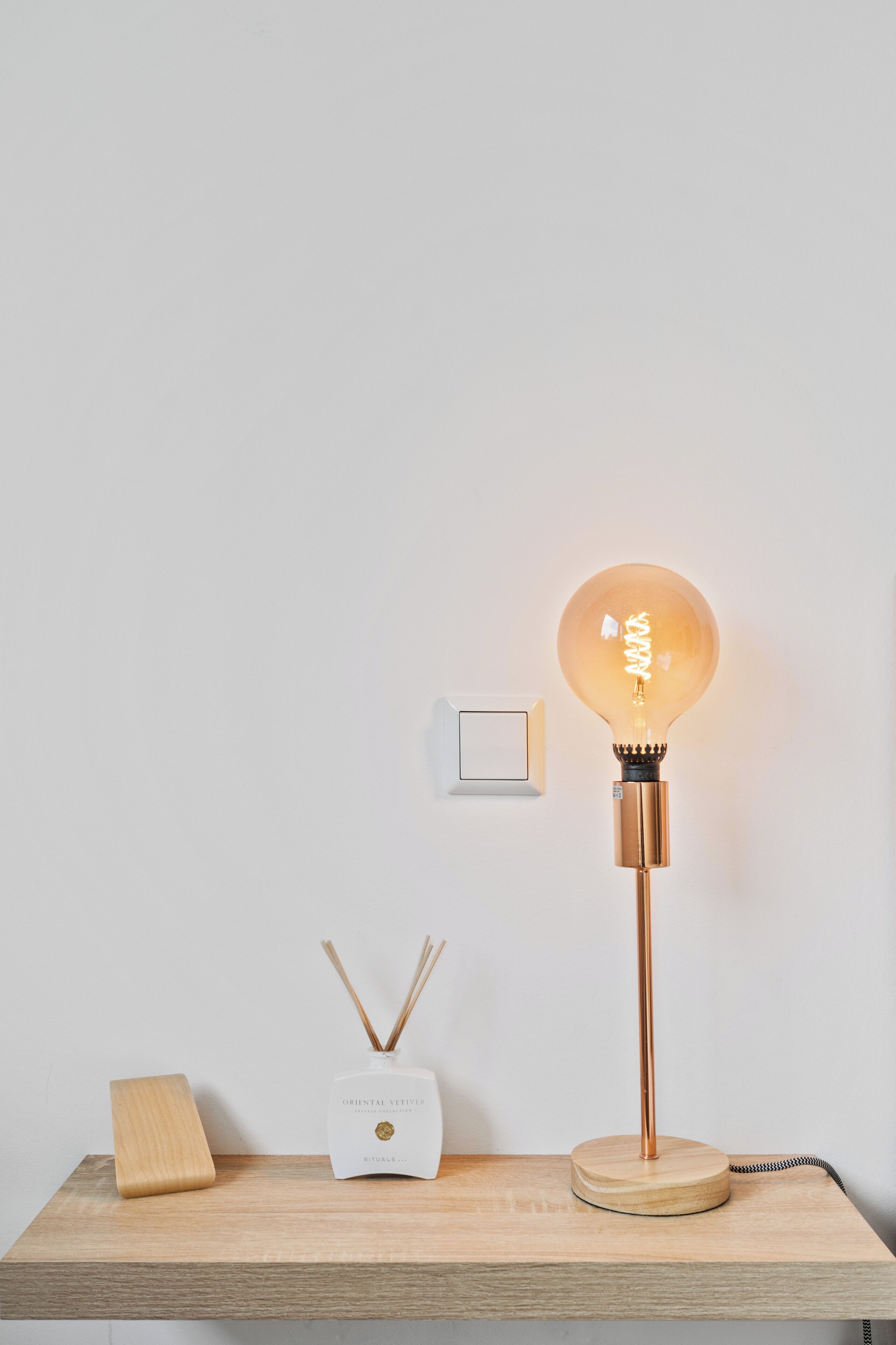 Une table en bois, une lampe, un diffuseur et un interrupteur au mur.