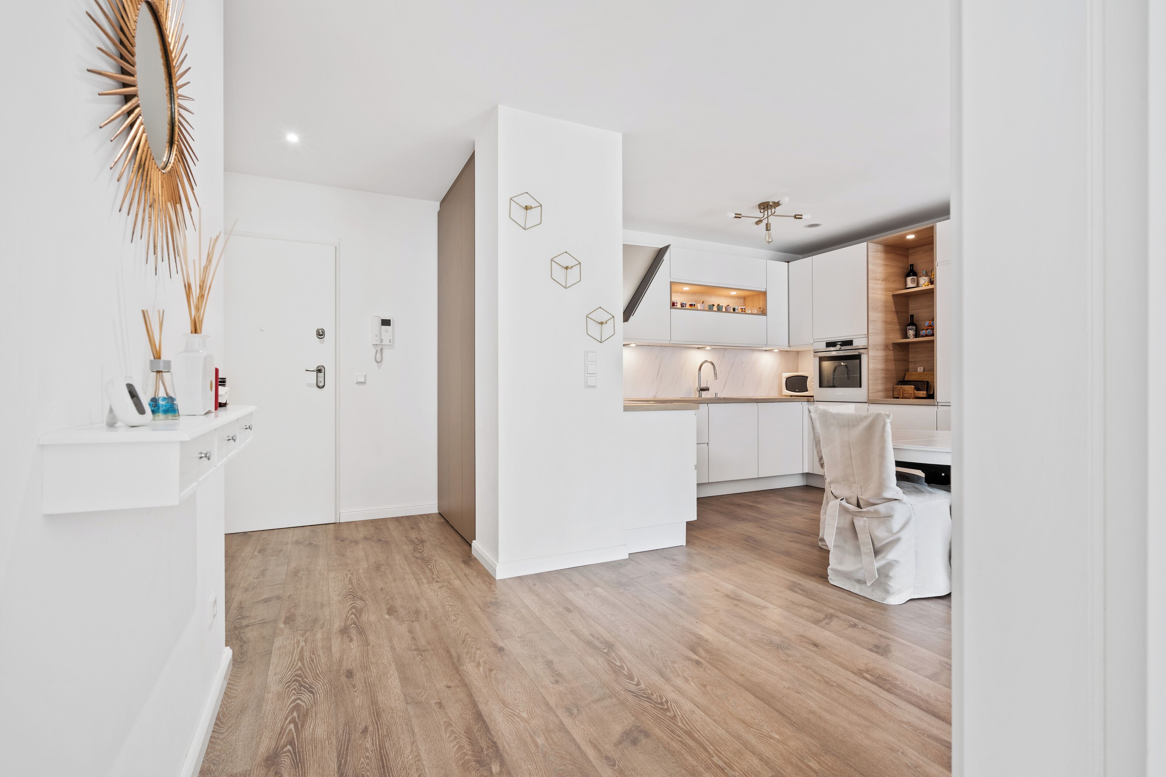 A modern kitchen with white cabinetry, a wooden floor, and a central island.