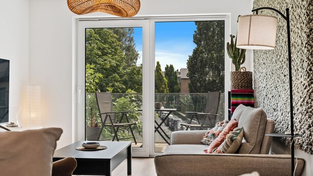 A modern living room with a sofa, a table, and a large window with a view of greenery and a street. - Stylish Apt Bouneweg-Süd Book Now ID225 (Luxembourg City)