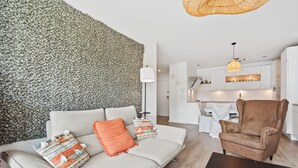 A modern living room with a textured wall, a sofa with cushions, a brown armchair, and a dining area in the background. - Stylish Apt Bouneweg-Süd Book Now ID225 (Luxembourg City)