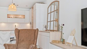 A modern kitchen with white cabinetry, a brown chair, a wooden-framed mirror, and a small easel with a painting. - Stylish Apt Bouneweg-Süd Book Now ID225 (Luxembourg City)