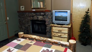 A room with a stone fireplace, a television on a wooden stand, a Christmas tree, and a quilt on the bed.
