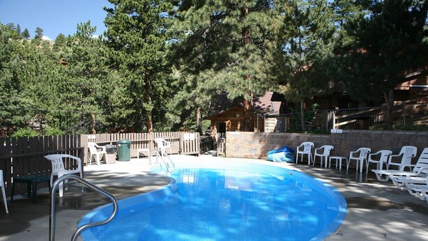 A swimming pool with a diving board, surrounded by white plastic chairs and a stone wall.